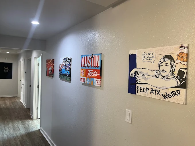 A long hallway featuring several colorful, contemporary paintings illuminated by recessed ceiling lights.