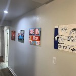 A long hallway featuring several colorful, contemporary paintings illuminated by recessed ceiling lights.