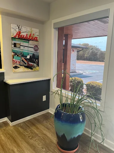 A bright corner of a room with a large window, a blue decorative planter, and a vibrant painting on the wall.