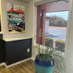 A bright corner of a room with a large window, a blue decorative planter, and a vibrant painting on the wall.