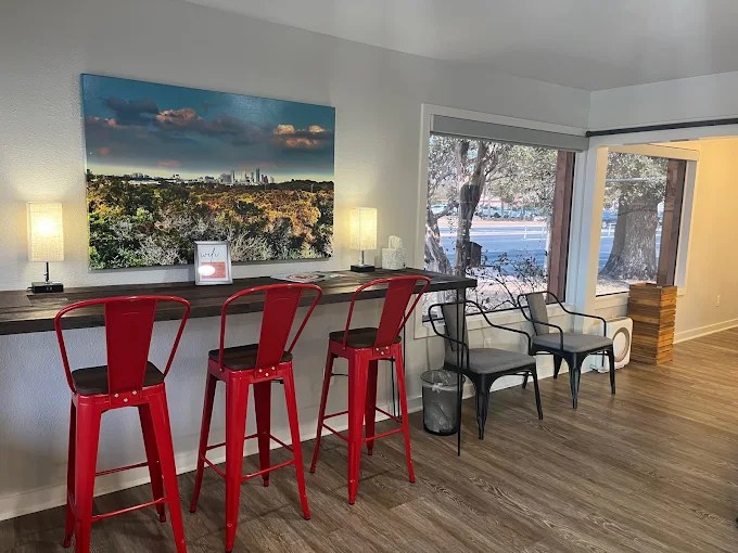 A high-top wooden counter with red metal stools, situated under a large piece of colorful wall art in a brightly lit room