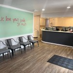 A view of the waiting area featuring a row of modern grey chairs against a light green wall, with the reception desk in the background.