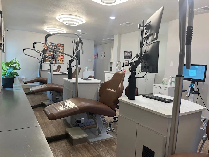 A modern dental operatory featuring a brown leather patient chair, advanced overhead lighting, and digital monitors.
