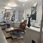 A modern dental operatory featuring a brown leather patient chair, advanced overhead lighting, and digital monitors.