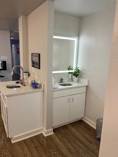 A small, clean restroom area with a white vanity, large mirror, and bright lighting.