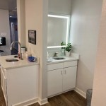 A small, clean restroom area with a white vanity, large mirror, and bright lighting.